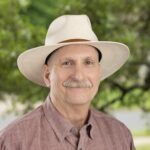 Headshot of John Palmer, a man in his 50's with a grey mustache and a white Stetson hat
